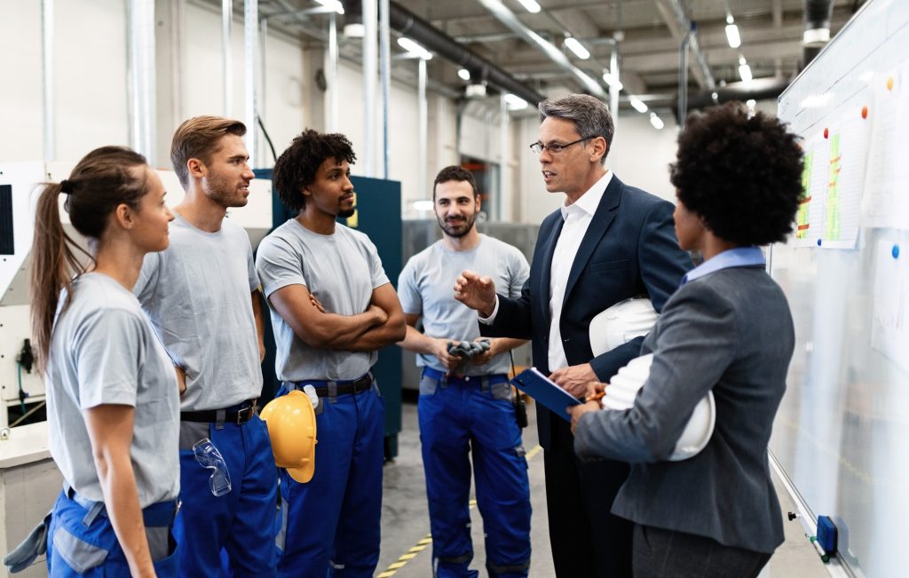 Mature businessman communicating with team of workers in a factory.